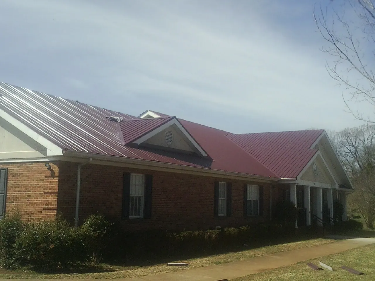 Red metal roof with gabled entries on a long brick building, from a Hail Damage Roof Repair job in Stephentown