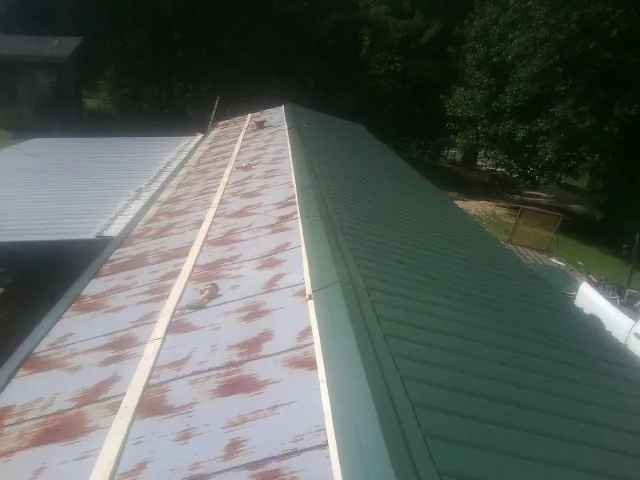 Old rusted panels beside newly installed green metal roofing — Wind Damage Roof Repair by Roofing Brothers in Stephentown