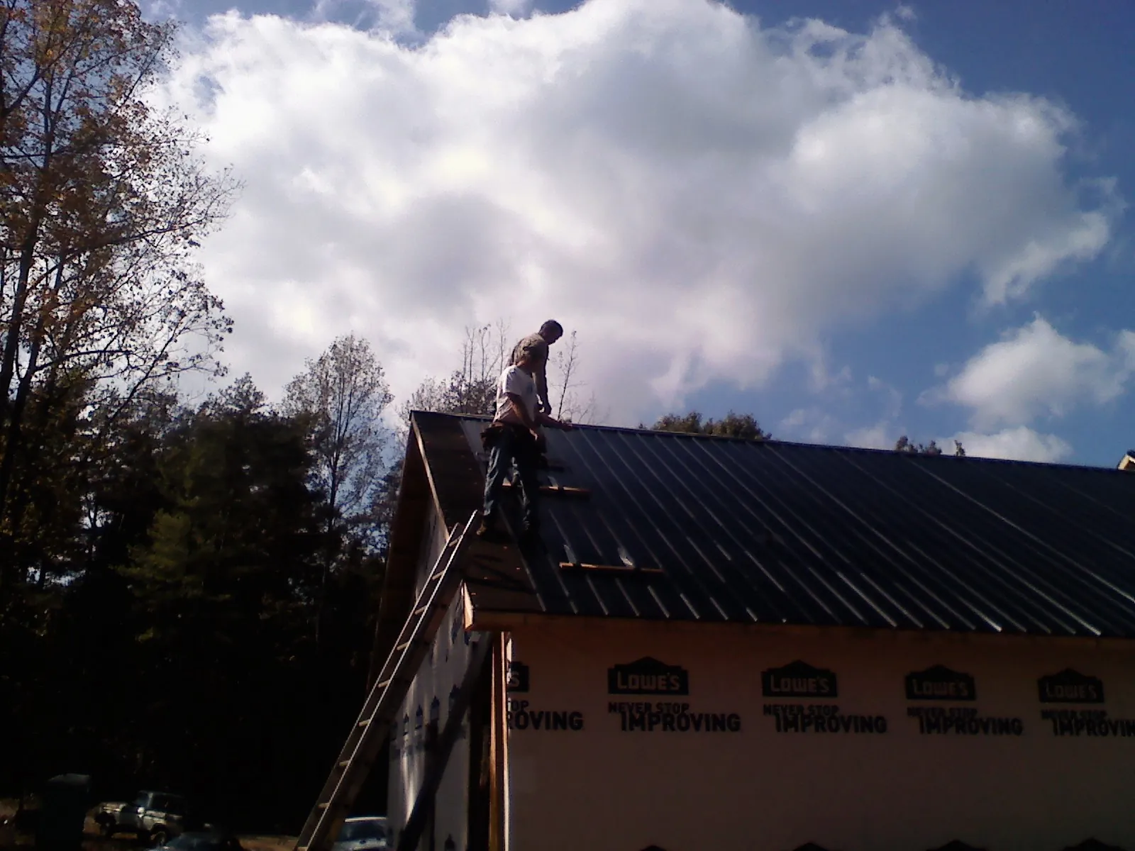 Roofer fastening dark metal panels high against a cloudy sky, from a Roof Inspection job in Stephentown
