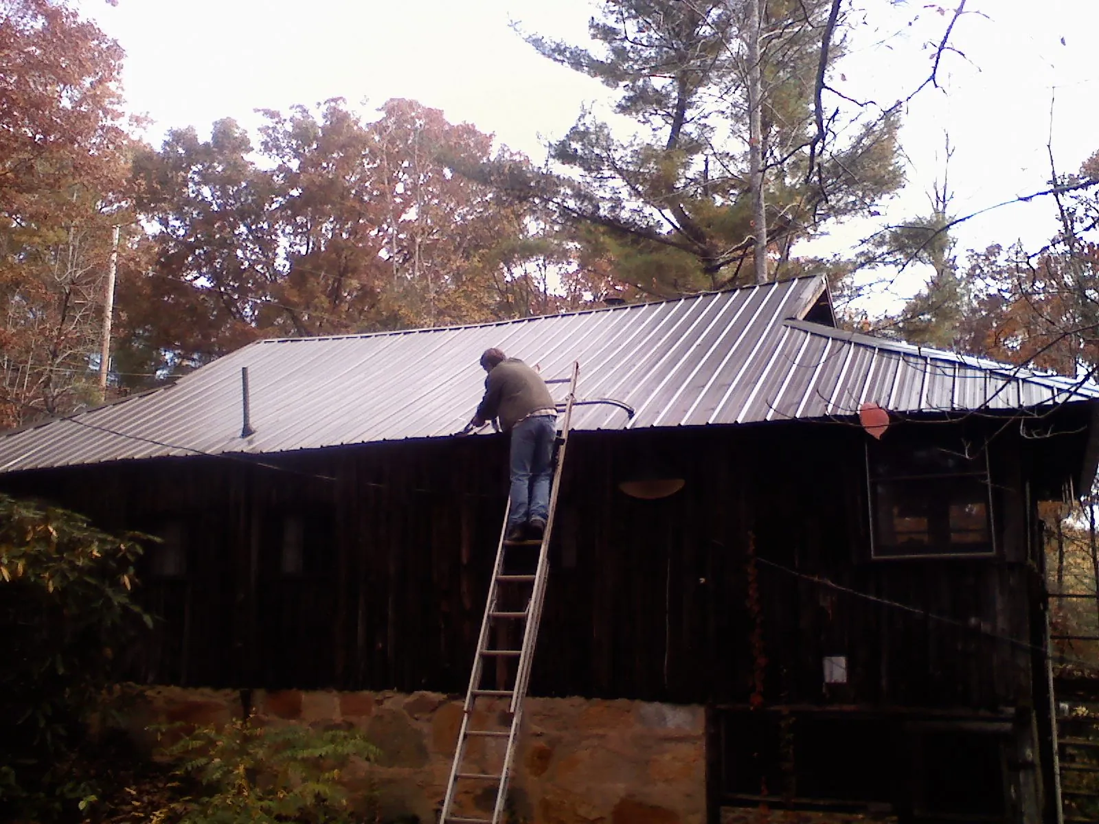 Roofer on a ladder working along the edge of a cabin metal roof in Stephentown