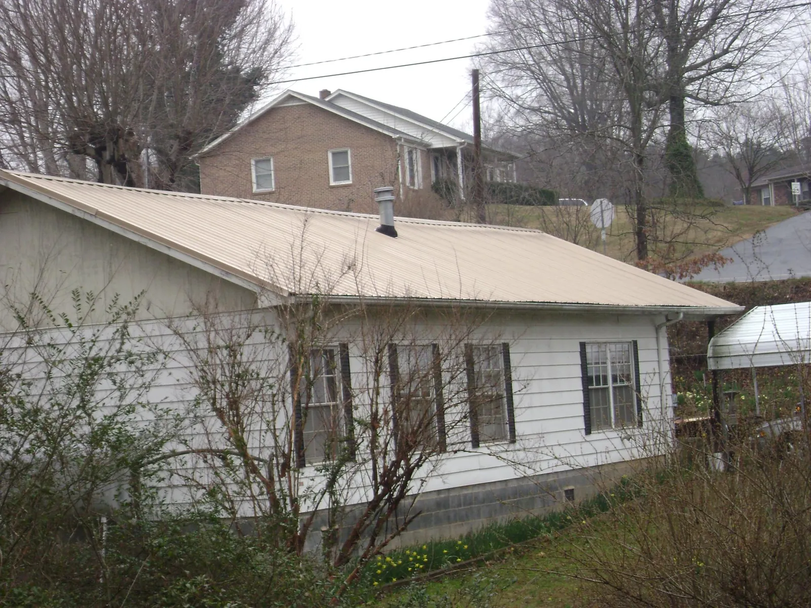 Tan metal roof on a white sided house set into a hillside — Commercial Roofing by Roofing Brothers in Stephentown